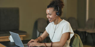 A professional woman sitting at a desk, wearing a headset with a microphone, actively participating in an online web call