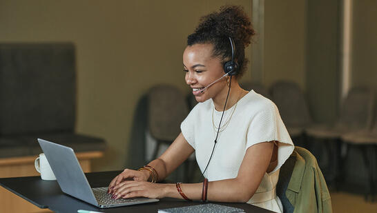 A professional woman sitting at a desk, wearing a headset with a microphone, actively participating in an online web call