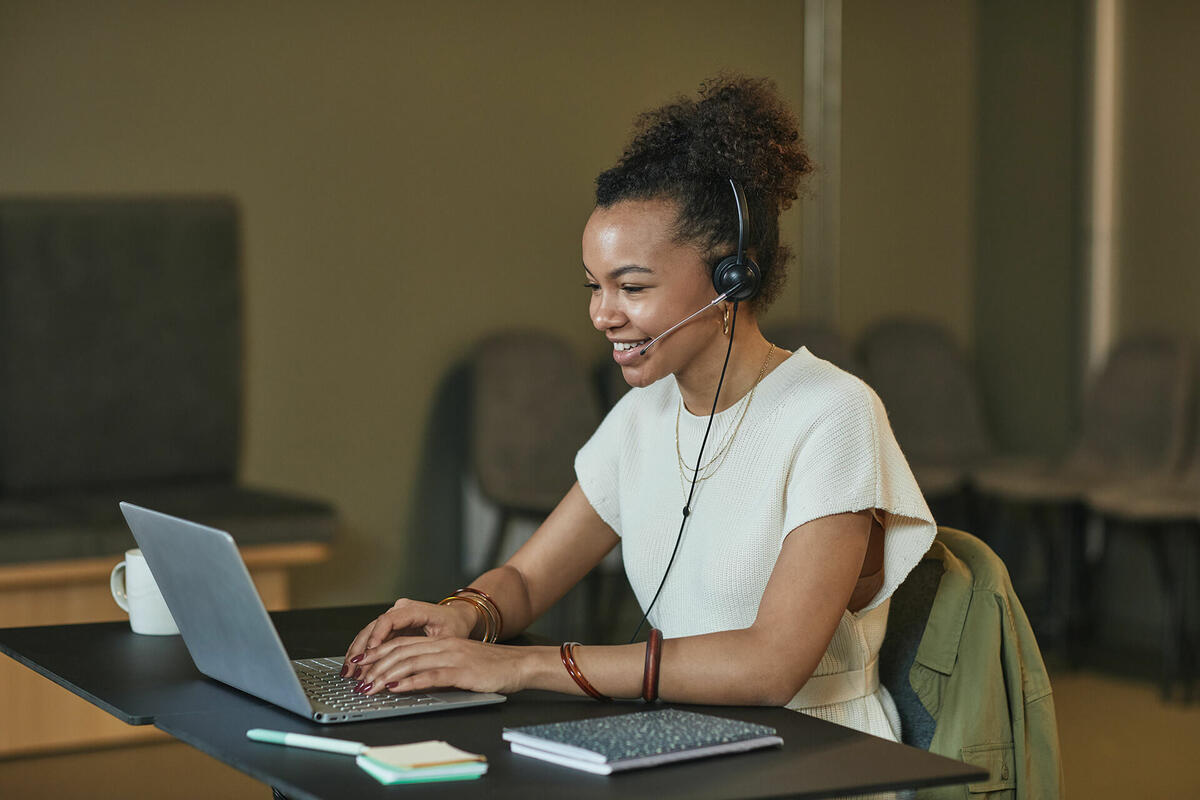  A professional woman sitting at a desk, wearing a headset with a microphone, actively participating in an online web call