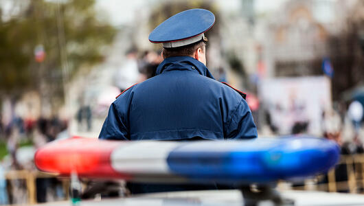 Back view of a policeman standing near a partially visible police car, representing emergency services in action